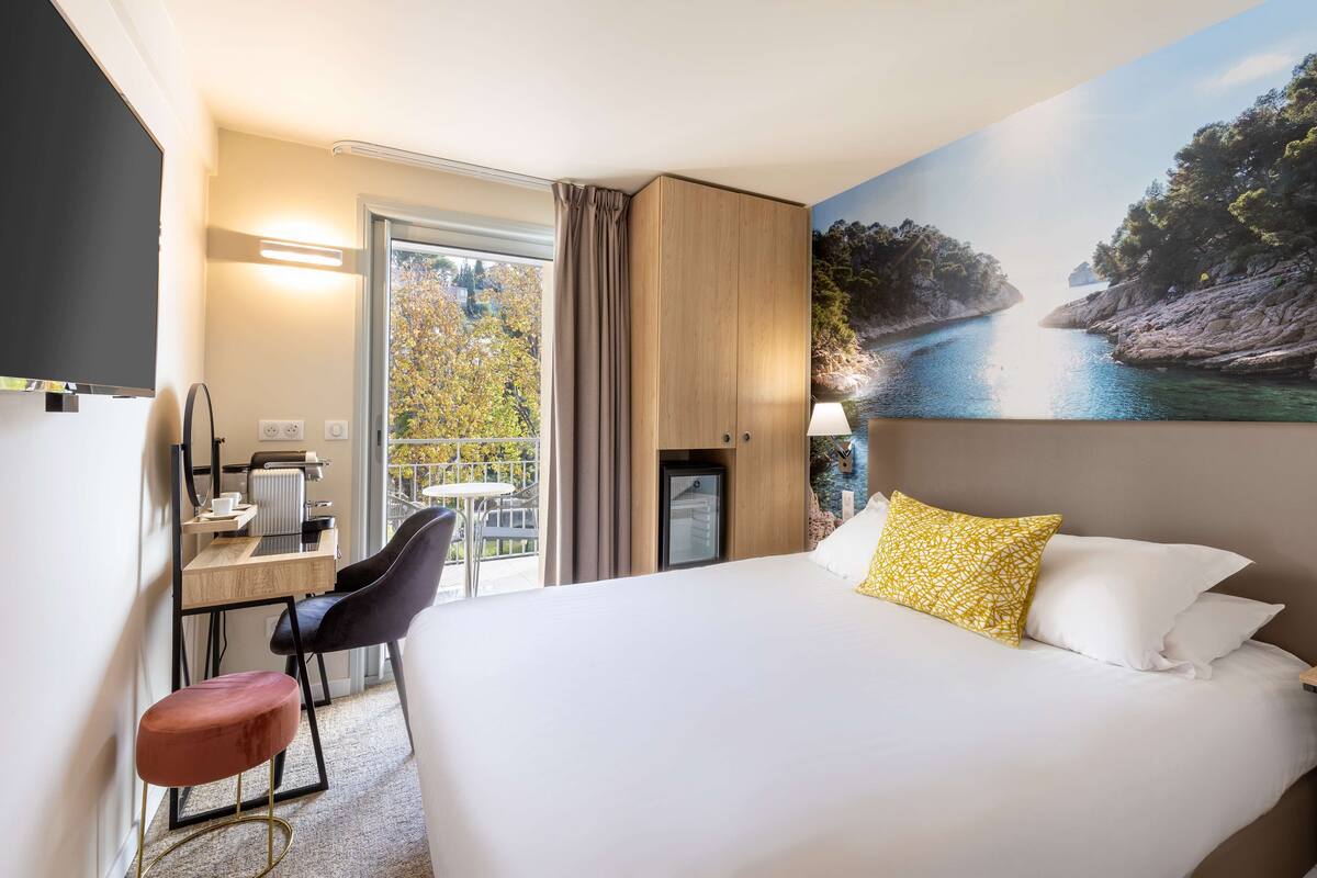Une chambre d’hôtel comprenant un lit, un bureau avec une chaise, une petite table, un radiateur et une vue sur un paysage naturel.