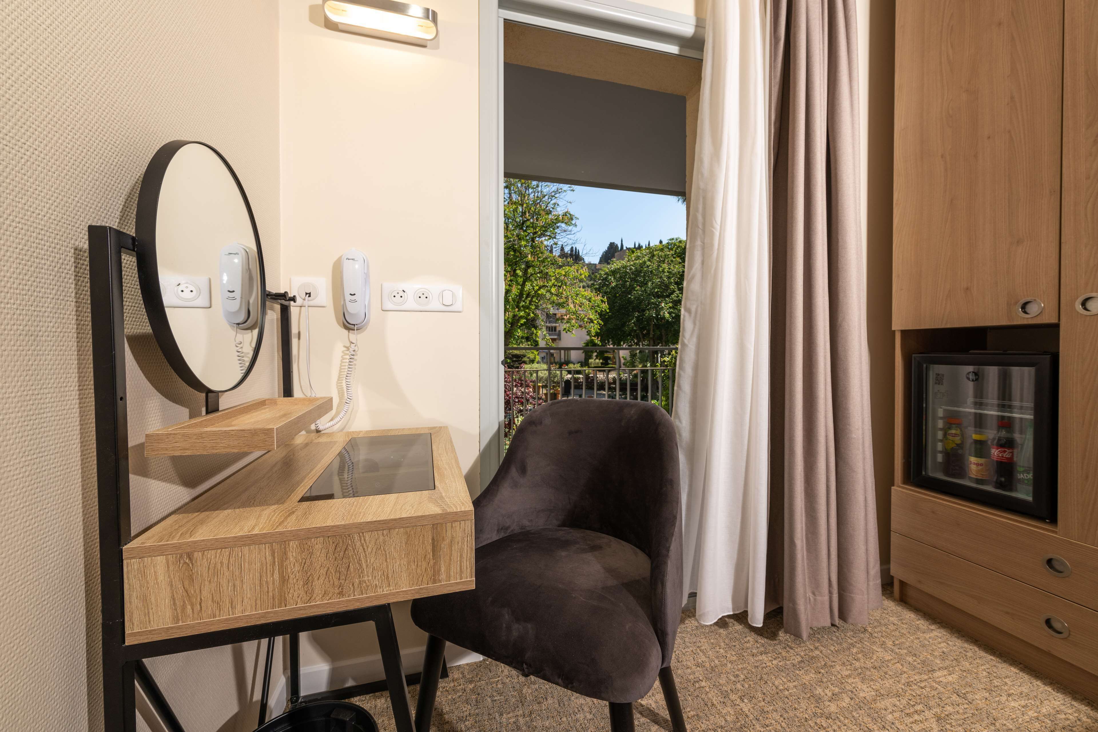 A room with a wooden desk, a black chair, a mirror, and a minibar.