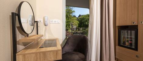 A room with a wooden desk, a black chair, a mirror, and a minibar.
