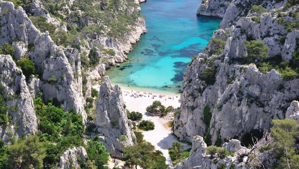 Un paisaje costero con acantilados rocosos, aguas turquesas cristalinas y una playa de arena.