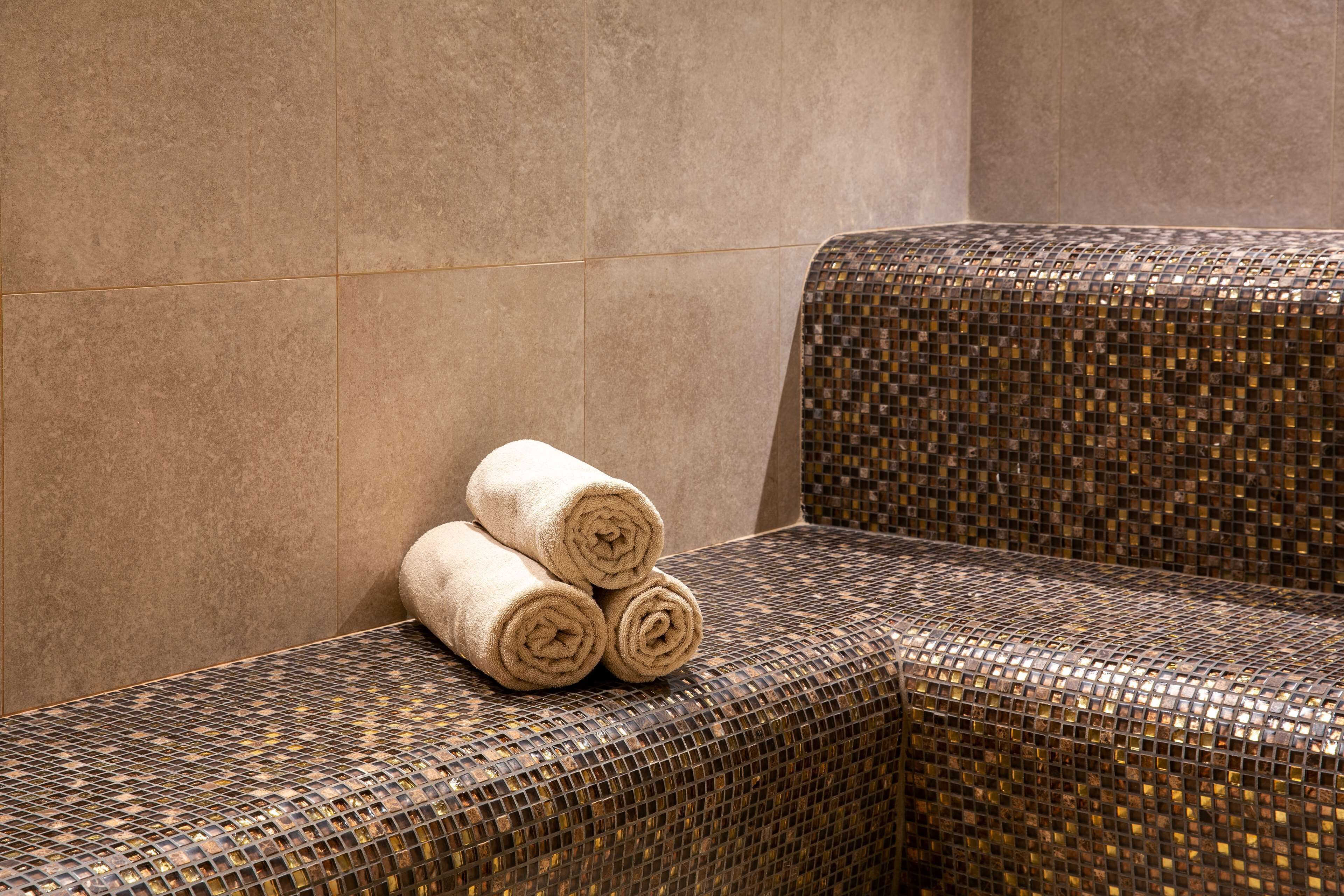 Un coin de pièce avec un banc à motifs en mosaïque et à texture particulière, et un mur orné d’un motif similaire.