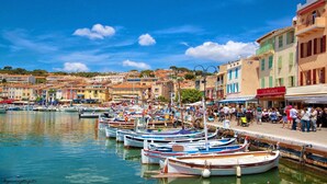 Un pueblo costero con barcos amarrados a lo largo del muelle, edificios con comercios y un cielo azul despejado.