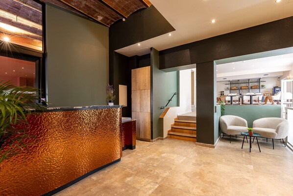 A reception area with a textured counter, a staircase leading to a bar area, and two chairs with a small table. - Best Western Hotel & SPA Coeur De Cassis (Cassis)