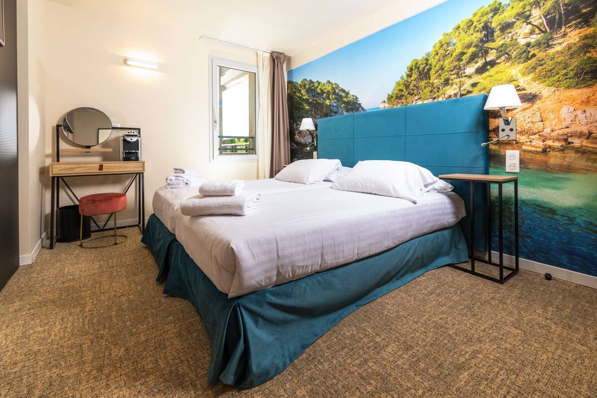 Une chambre d’hôtel avec un lit, un bureau doté d’un miroir, une chaise et une vue sur un paysage côtier.