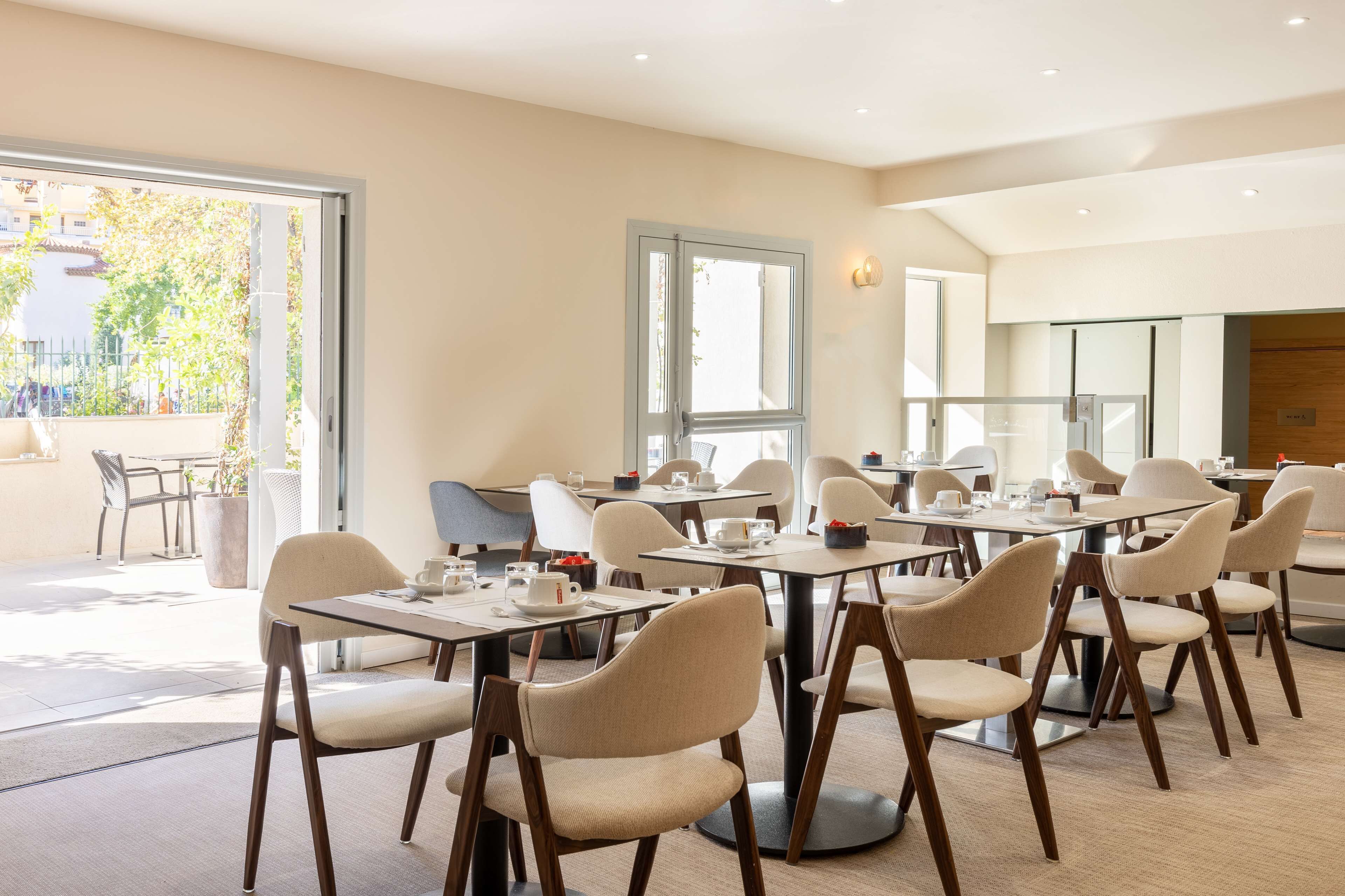 Un comedor moderno con mesas redondas y sillas color beige, ventanas amplias y vistas al exterior.