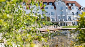 A multi-story hotel with a red-tiled roof, a swimming pool, and a landscaped garden area. - Landhotel Rügheim (Hofheim in Unterfranken)