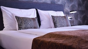 Un lit bien fait, avec du linge de lit blanc et des coussins à motifs, une tête de lit sombre et une lampe moderne placée à côté.