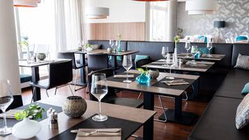 Un restaurante moderno con varias mesas, asientos en tonos grises y negros, e iluminación colgante.