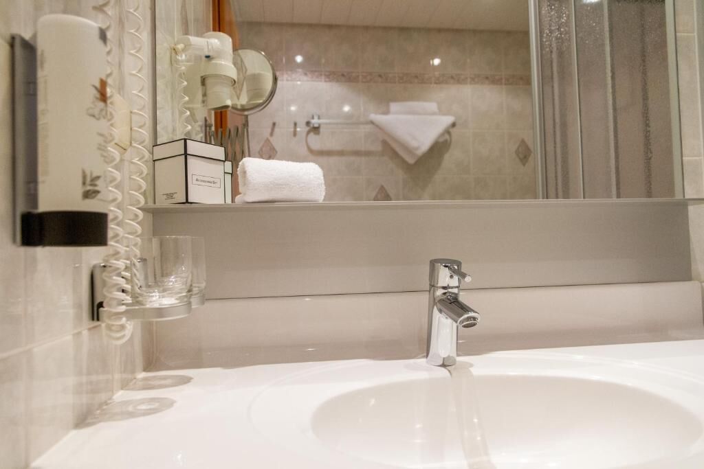 A bathroom with a white sink, a mirror, a towel rack, and a glass soap dispenser.