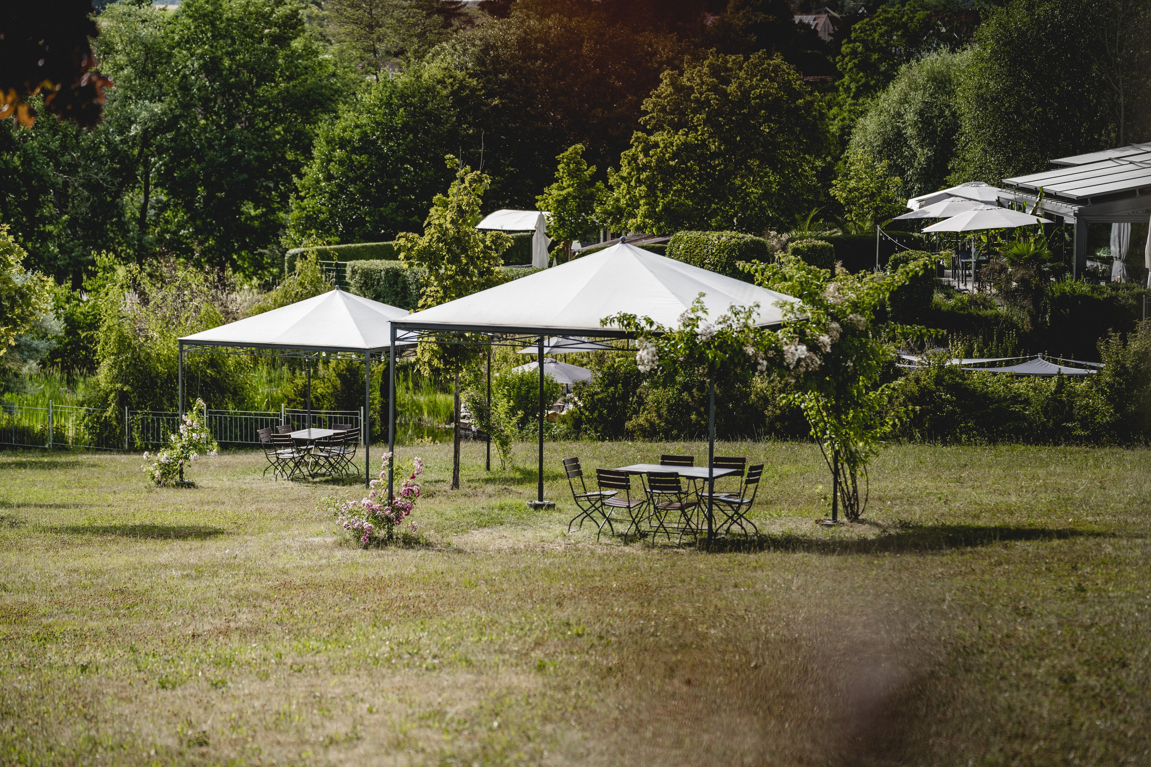 Un espacio al aire libre con césped, una carpa blanca, mesas y sillas.