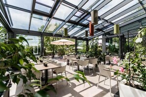 An indoor garden with tables and chairs, glass ceiling, and potted plants. - Landhotel Rügheim (Hofheim in Unterfranken)