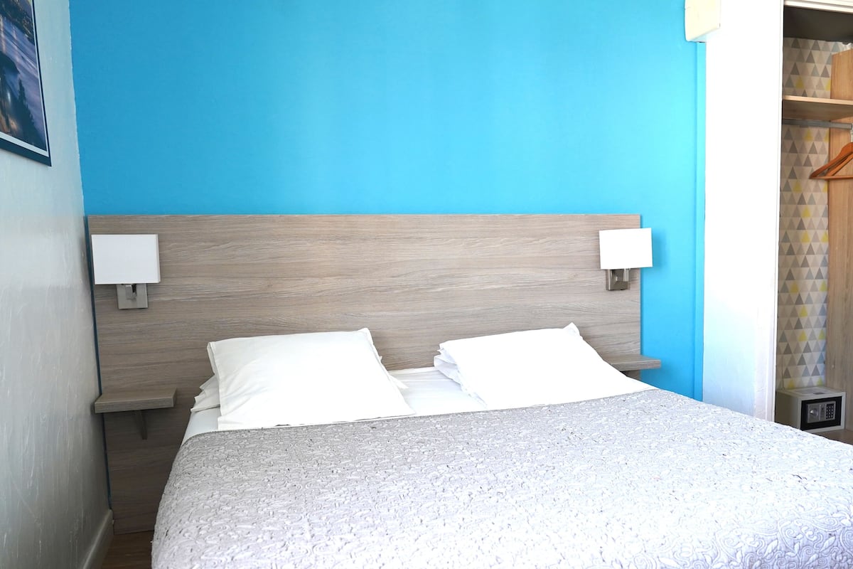 A neatly made bed with white linens in a room with a blue accent wall and a wooden headboard.