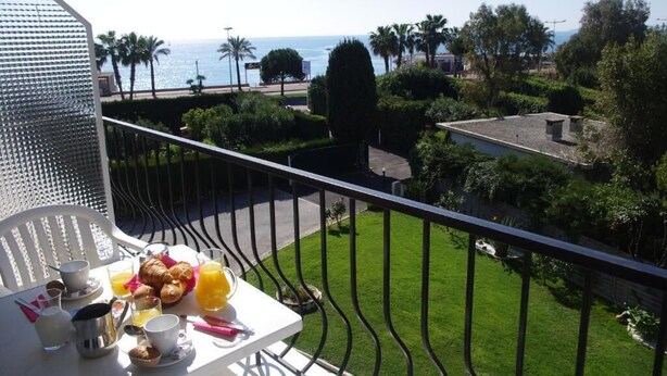 A balcony with a table set for breakfast, overlooking a well-maintained garden and a view of the sea. - MOTEL ASCOT - Hôtel & Appartements (Cagnes-sur-Mer)
