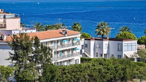 A coastal hotel with multiple balconies, a view of the sea, and a lighthouse in the background. - MOTEL ASCOT - Hôtel & Appartements (Cagnes-sur-Mer)