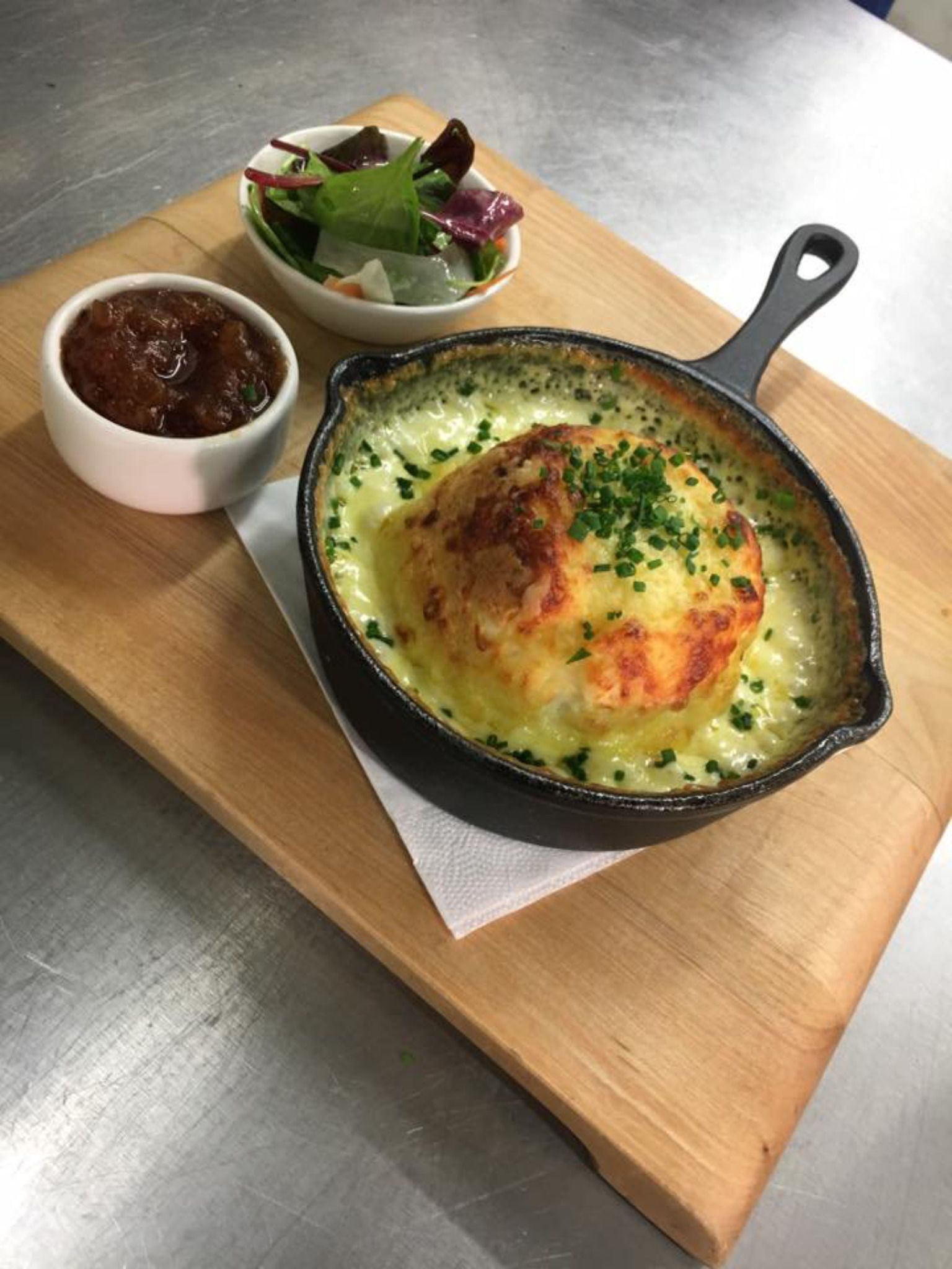 Una sartén con un plato dorado, un cuenco pequeño de salsa y una ensalada sobre una tabla de madera.