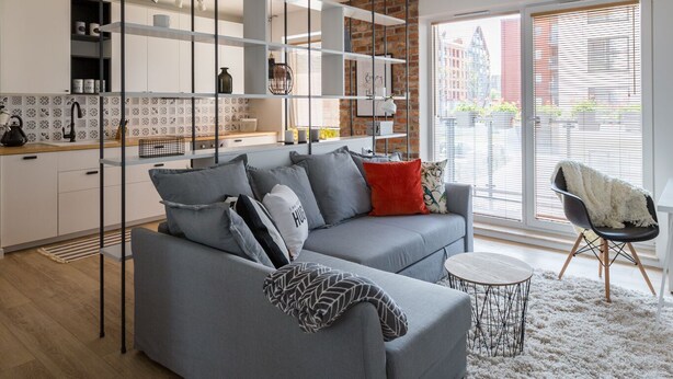 A modern living room with a grey sofa, a small round table, and a large window with blinds. - Dream Holiday-Apartamenty Chmielna Park (Gdansk)