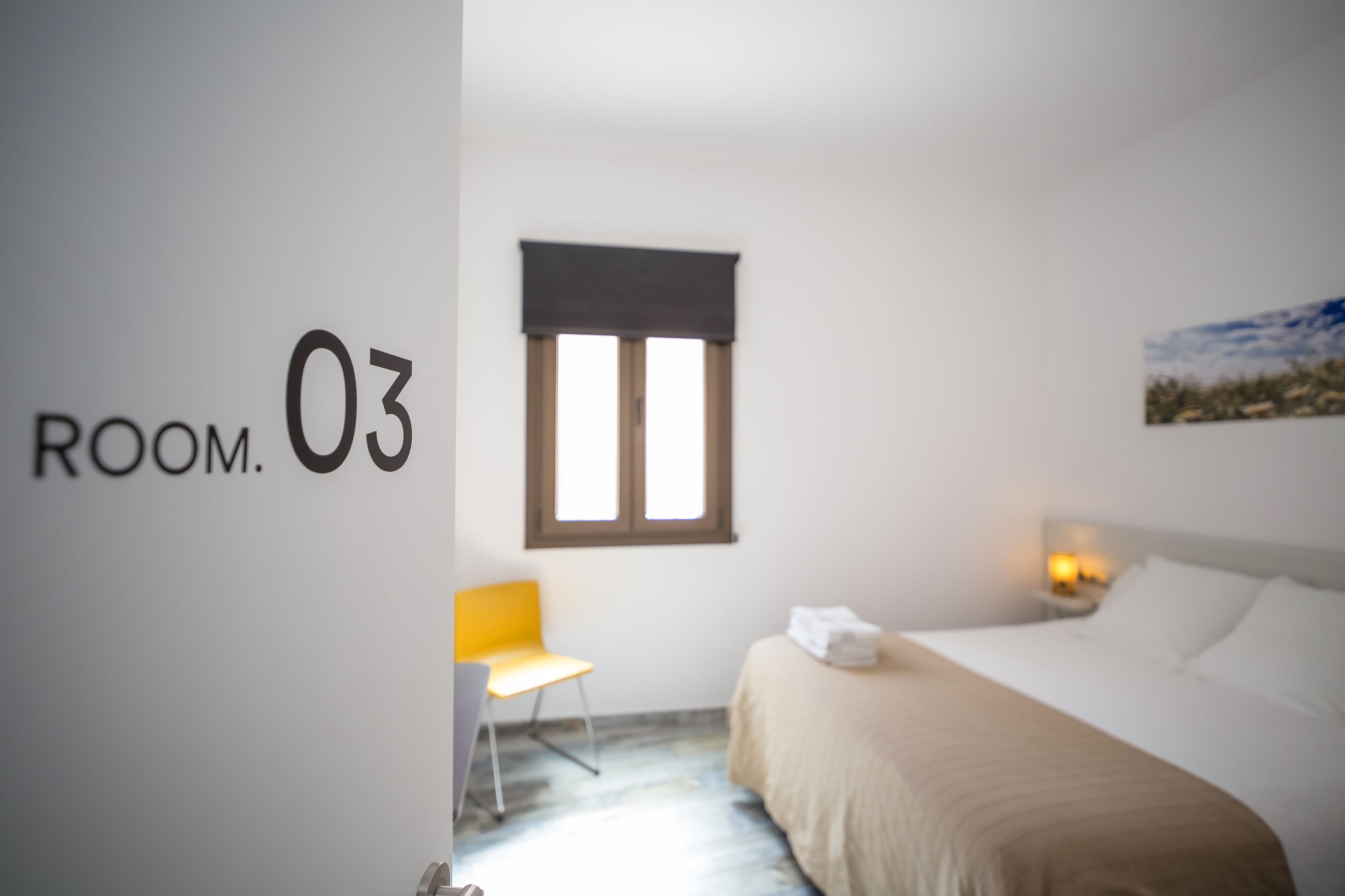 Une chambre d’hôtel équipée d’un lit, d’une chaise, d’une fenêtre et d’une plaque fixée au mur indiquant le numéro de la chambre.