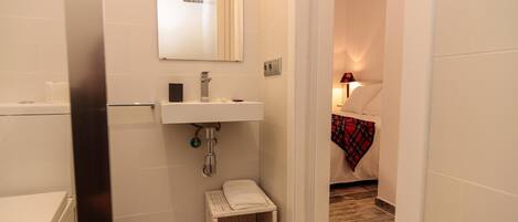Een badkamer met een wit wastafel, spiegel en toilet. Er ligt een klein mandje met schoenen en een handdoek op de vloer.