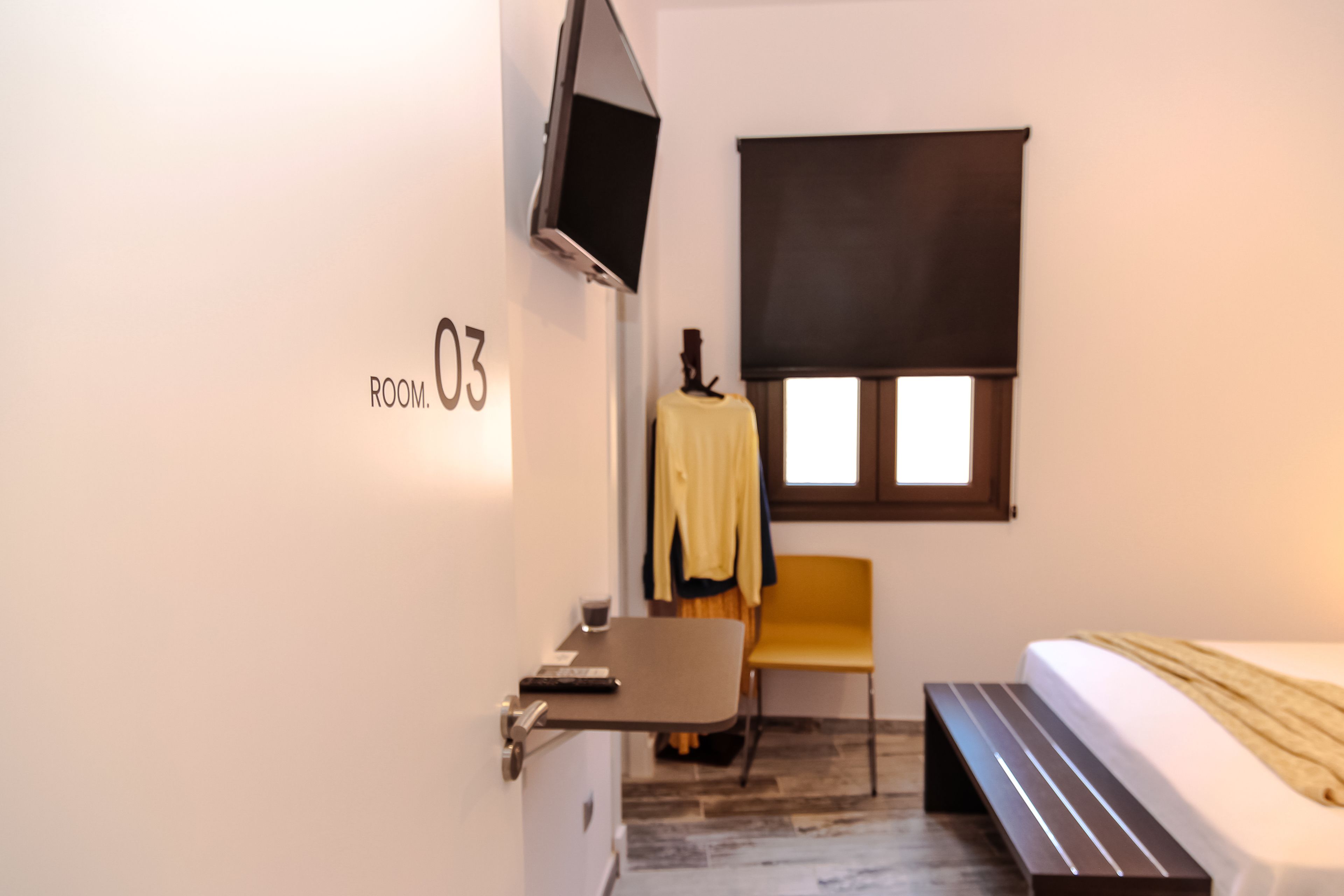 A hotel room with a bed, a desk, a chair, a TV mounted on the wall, and a window with a blind.