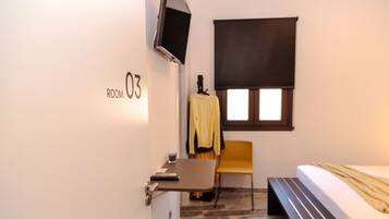A hotel room with a bed, a desk, a chair, a TV mounted on the wall, and a window with a blind.