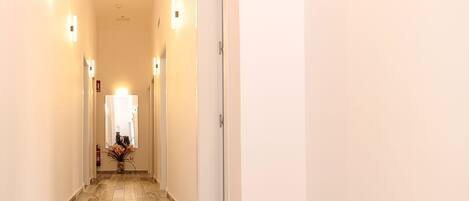 A hallway with a tiled floor, white walls, and light fixtures on the ceiling.
