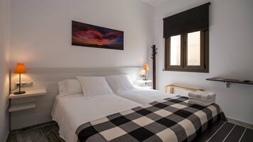 A hotel room with a bed, two bedside lamps, a painting, a window with a blind, and a small shelf.
