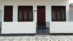 Un edificio con tres puertas y ventanas de madera oscura, paredes blancas y una entrada con baldosas.