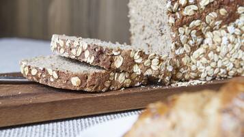 A loaf of whole grain bread with oats on a wooden cutting board.
