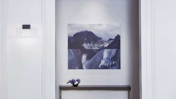 A framed photograph of a mountain landscape with a small vase of flowers on a console table below. - Messori Suites (Florence)