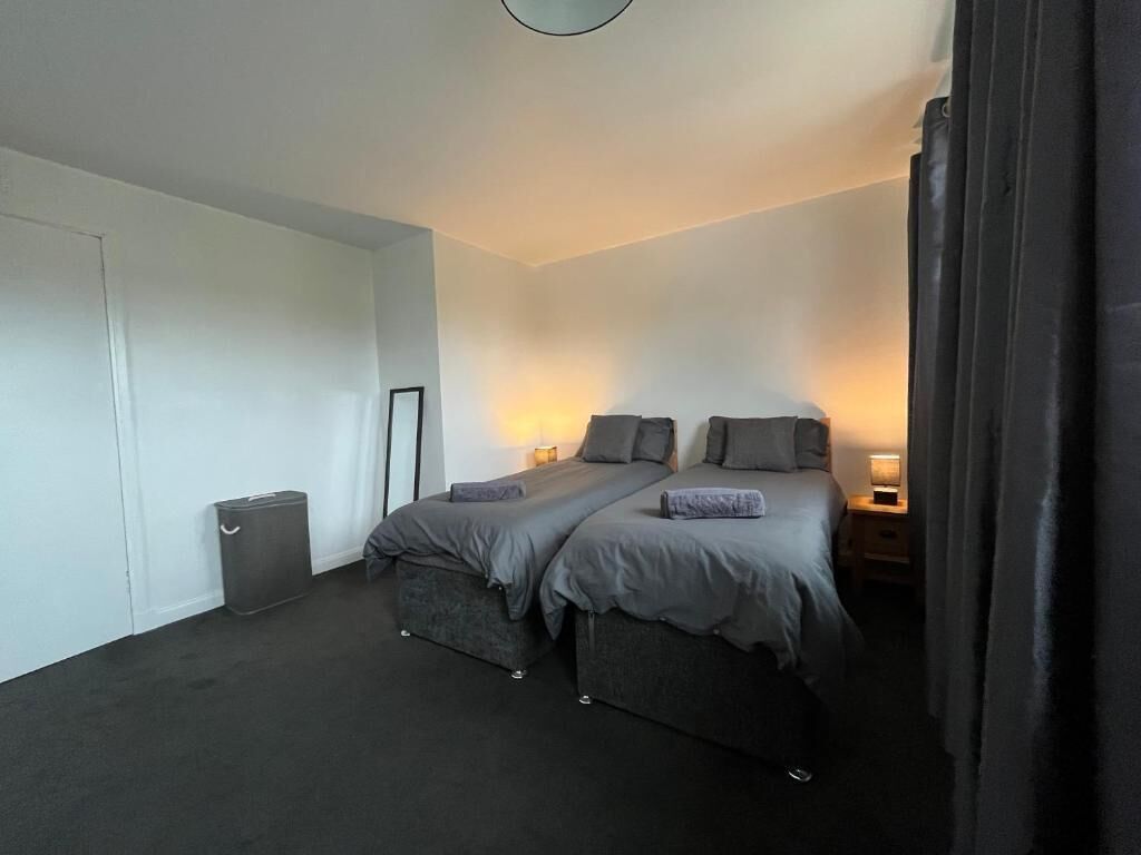 A bedroom with two beds, a small trash bin, and a nightstand with a lamp.