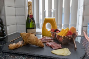 A breakfast setup with croissants, cheese, fruits, and a bottle of champagne on a slate board. - London Heathrow Serviced Apartments (Staines)