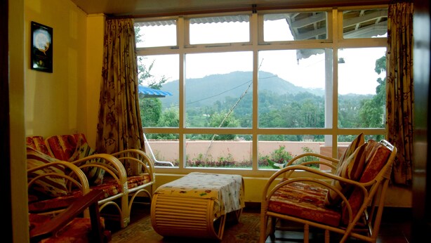 Una habitación con un ventanal grande, muebles de mimbre y una pequeña mesa.