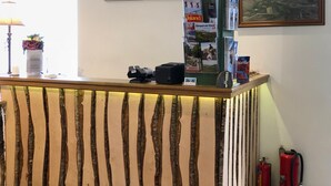 Una mesa de recepción con diseño de listones de madera, una lámpara, un jarrón con flores, cuadros enmarcados en la pared y un extintor.