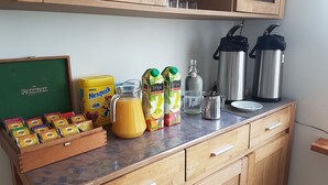 Una encimera de cocina con diversos alimentos y bebidas, incluyendo un cartón de Nesquik, una jarra de jugo de naranja, una botella de Tropi y una cafetera.