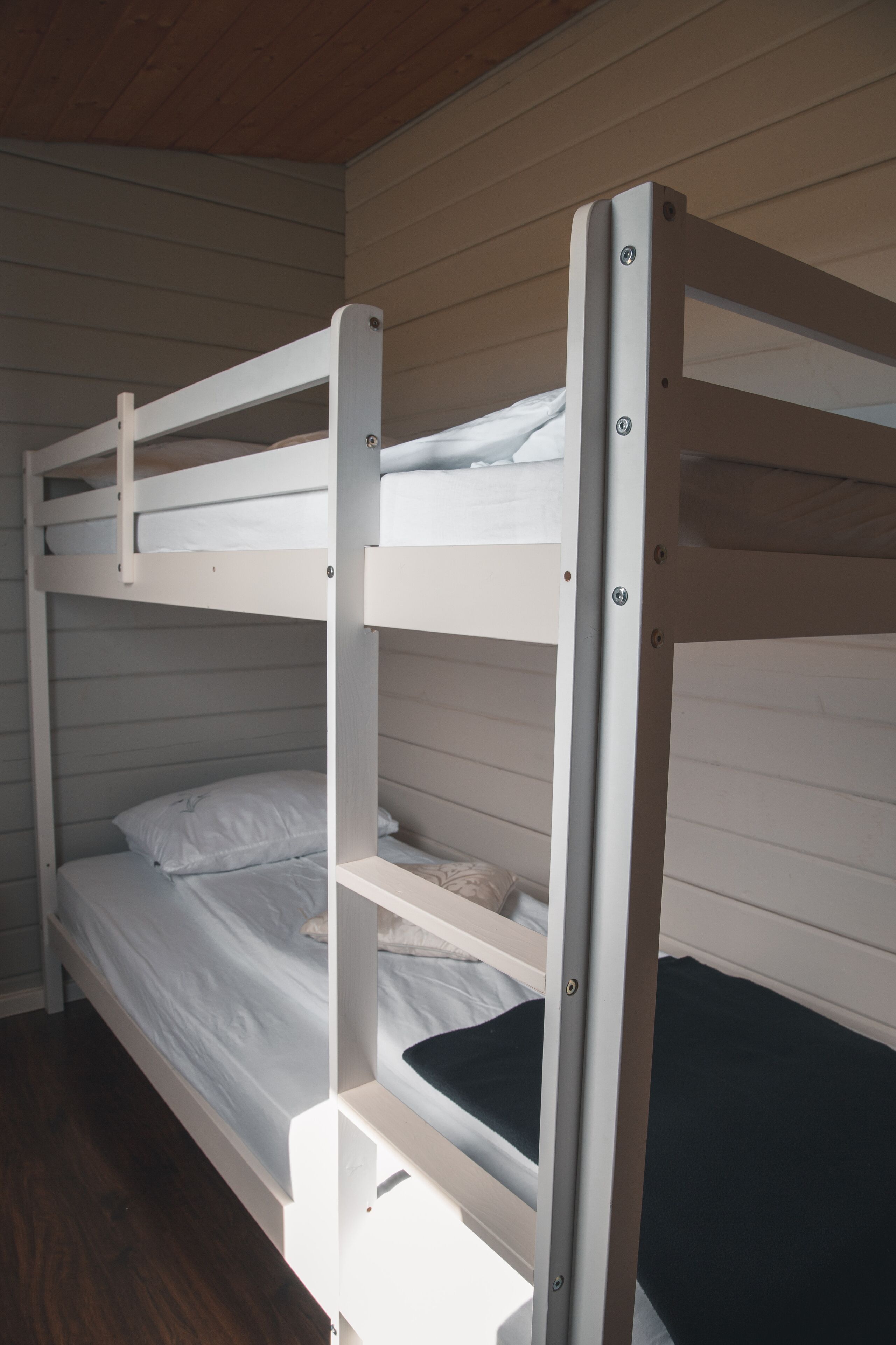 A bunk bed with white bedding and a black mattress at the bottom bunk.