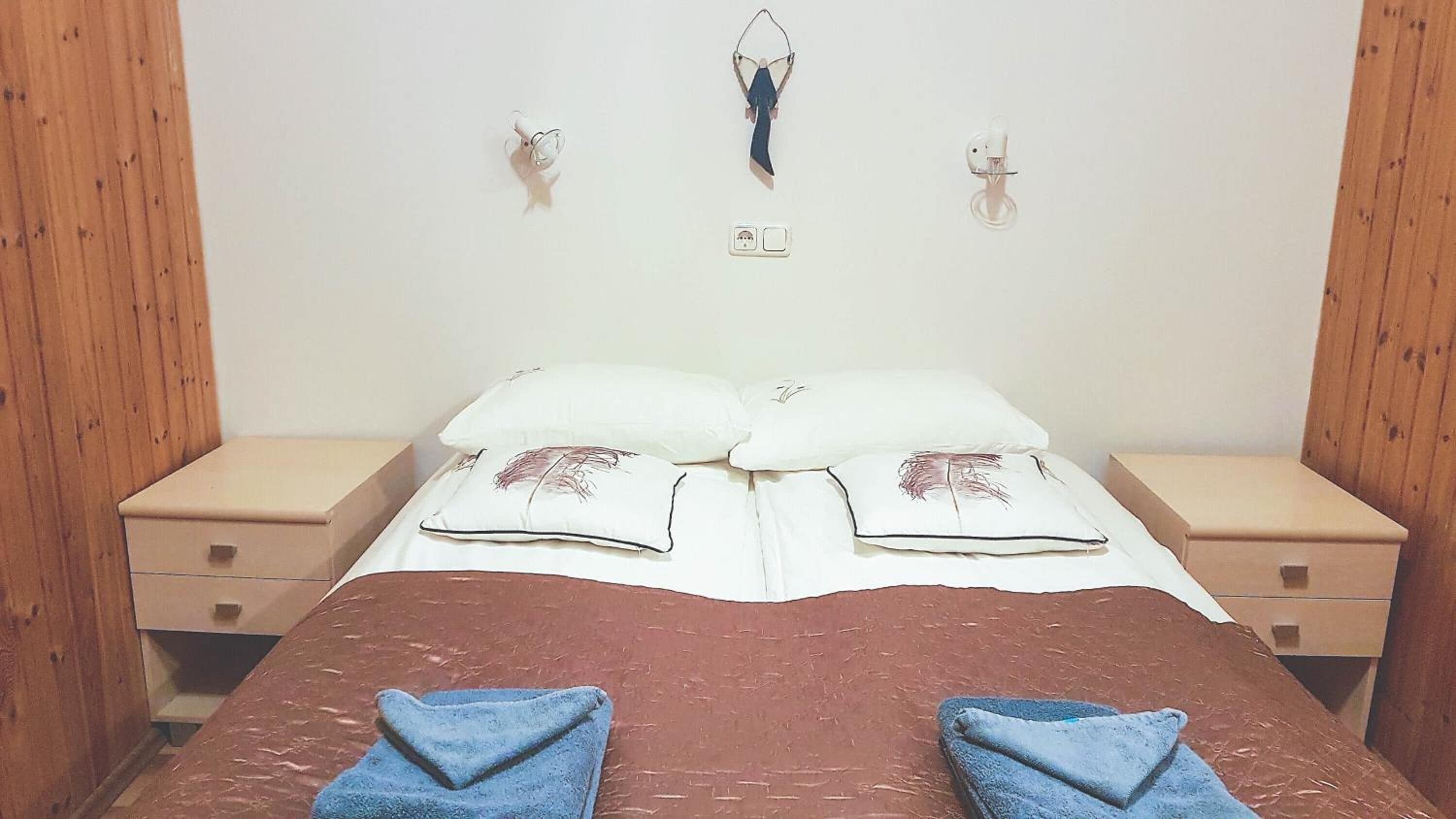 Um quarto com uma cama, duas mesas de cabeceira e uma luminária fixada na parede.