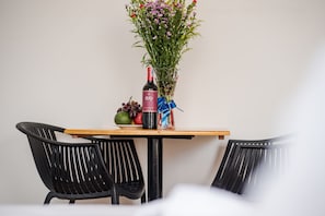 Une table à manger avec une bouteille de vin, un bouquet de fleurs et quelques fruits.