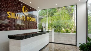 A reception area with a modern design, featuring a reception desk, a large window with a view of greenery, and a wall with the text "Villa Silver Moon". - Silver Moon Villa Hoi An (Da Nang)