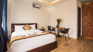 A hotel room with a bed, a small table with chairs, an air conditioning unit, and a wooden door. - Silver Moon Villa Hoi An (Da Nang)