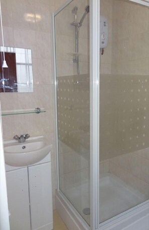 Un baño con ducha envuelta en vidrio, un lavabo blanco y una repisa de vidrio.