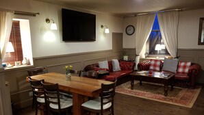 Una sala de estar acogedora con una mesa de comedor de madera, un sofá de cuero y un televisor instalado en la pared.