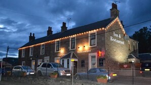 Un edificio de ladrillo con un letrero que dice "Tim & Restaurant" y una estructura pequeña adosada. Hay coches estacionados al frente.