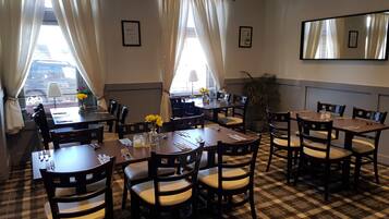 A dining area with multiple tables and chairs, large windows with curtains, and a checkered floor.