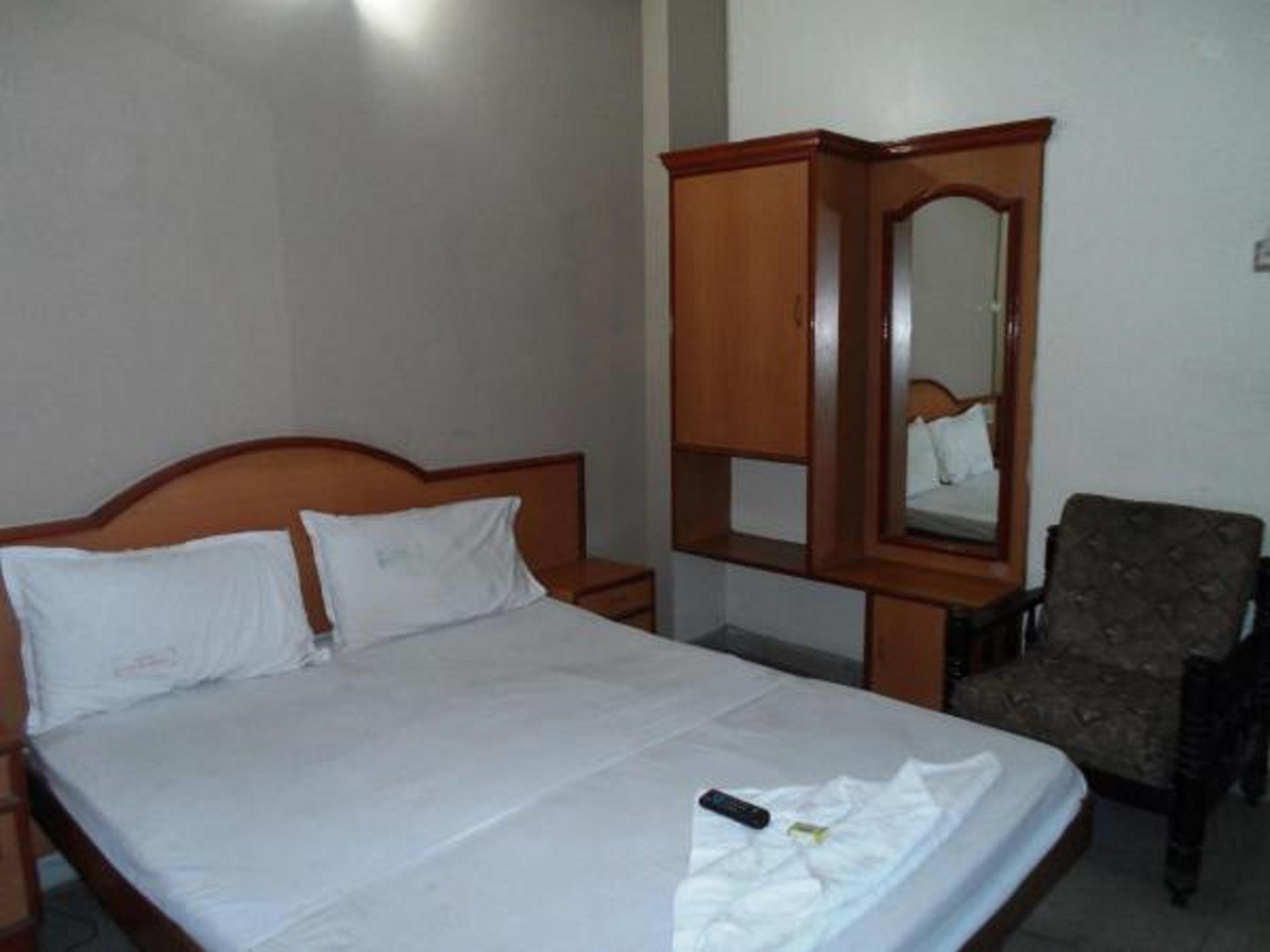 A bedroom with a wooden bed, a chair, and a mirror cabinet.