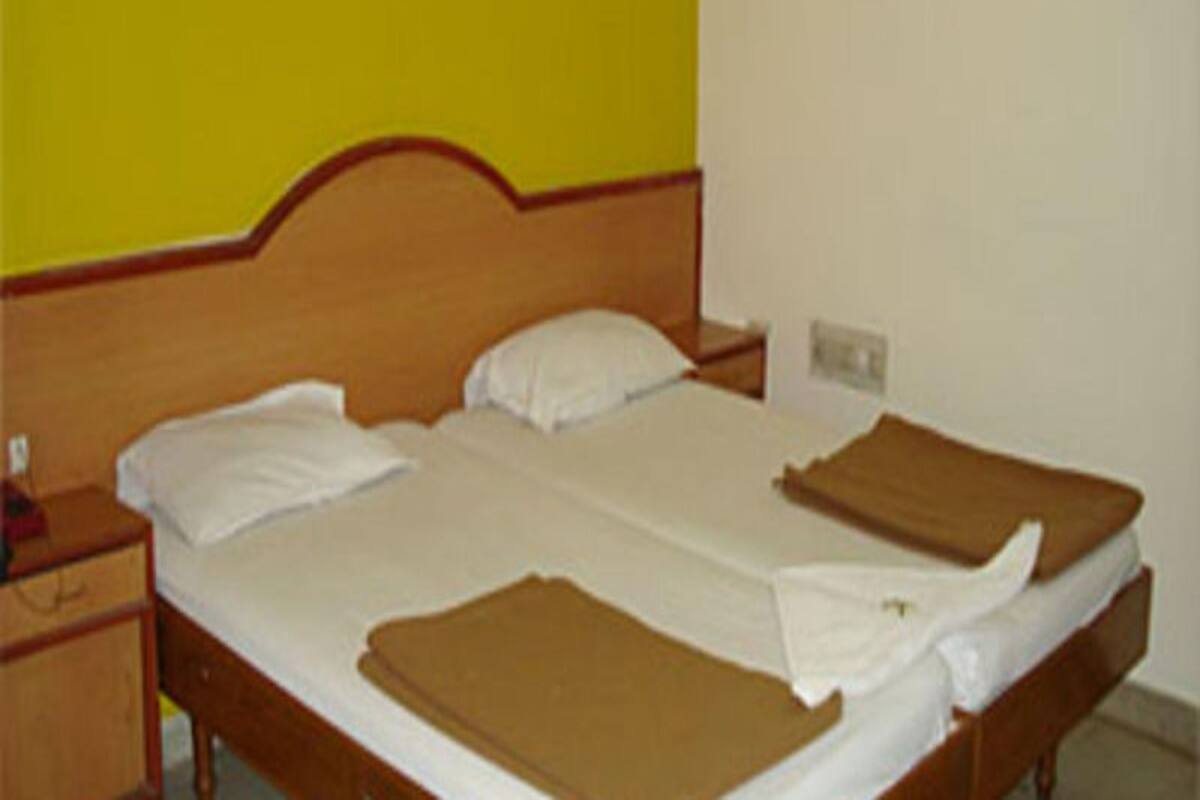 Una cama individual con cabecera de madera, ropa de cama blanca y una manta marrón.