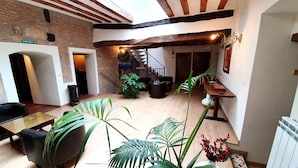 A spacious indoor area with exposed wooden beams, a staircase, and a variety of seating arrangements including a table and chairs. - Pensión Posada Ignatius (Navarrete)