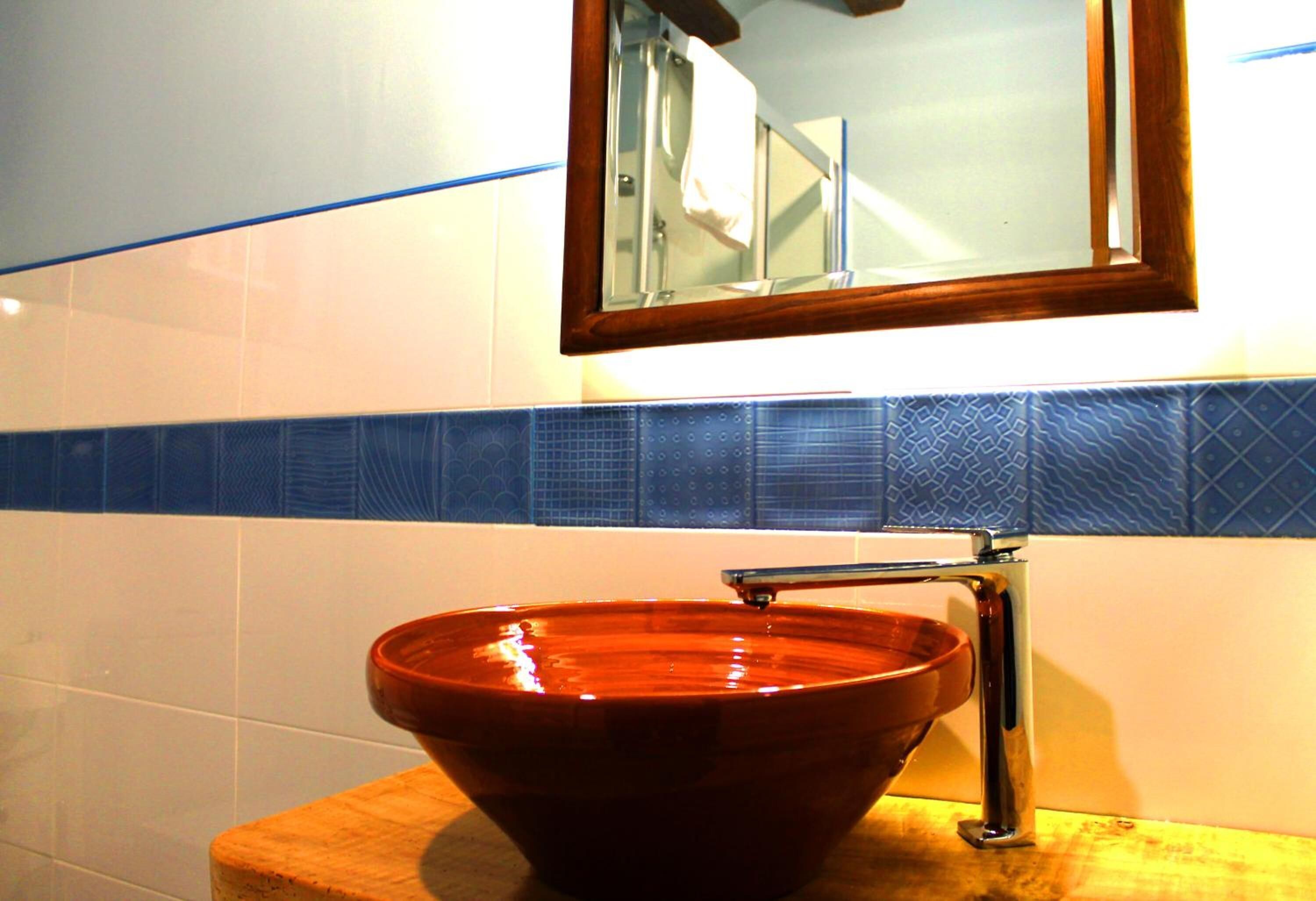 Un baño con tocador de madera, lavamanos de cerámica marrón y un espejo encima.
