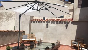 A sunlit patio with a glass table, potted plants, a wooden bench, and a large umbrella. - Pensión Posada Ignatius (Navarrete)