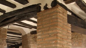 A room with exposed brick walls, stone arches, and wooden beams. There are two black chairs and a wooden table. - Pensión Posada Ignatius (Navarrete)