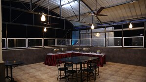 Une pièce spacieuse avec un plafond haut, de grandes fenêtres et une table centrale entourée de chaises.